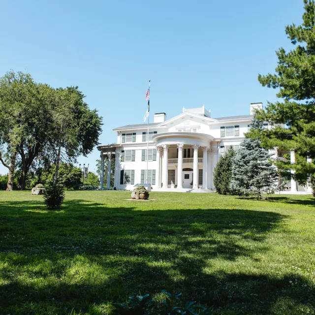 A large white mansion with a well-manicured lawn and a clear blue sky in the background.
