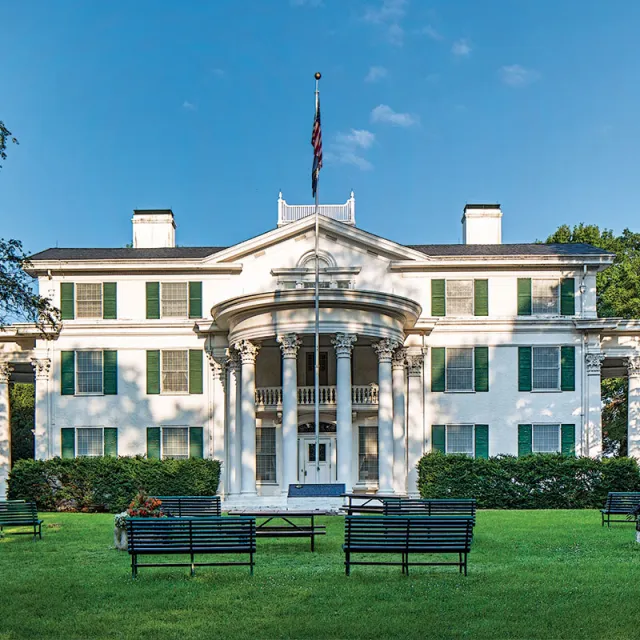 A large white mansion featuring green shutters, set against a clear blue sky.