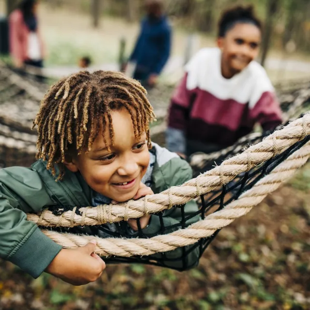 A young boy joyfully plays in a rope net, climbing and exploring with enthusiasm.