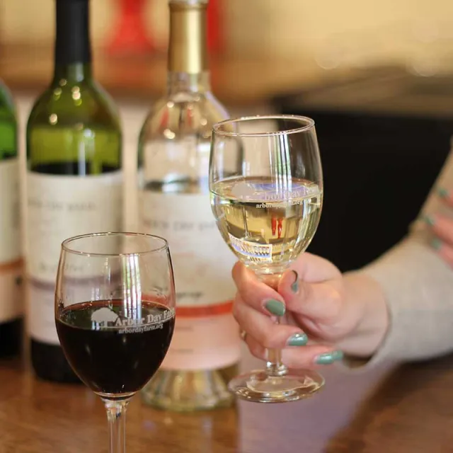 A woman holds a glass of wine, with various wine bottles displayed in the background.