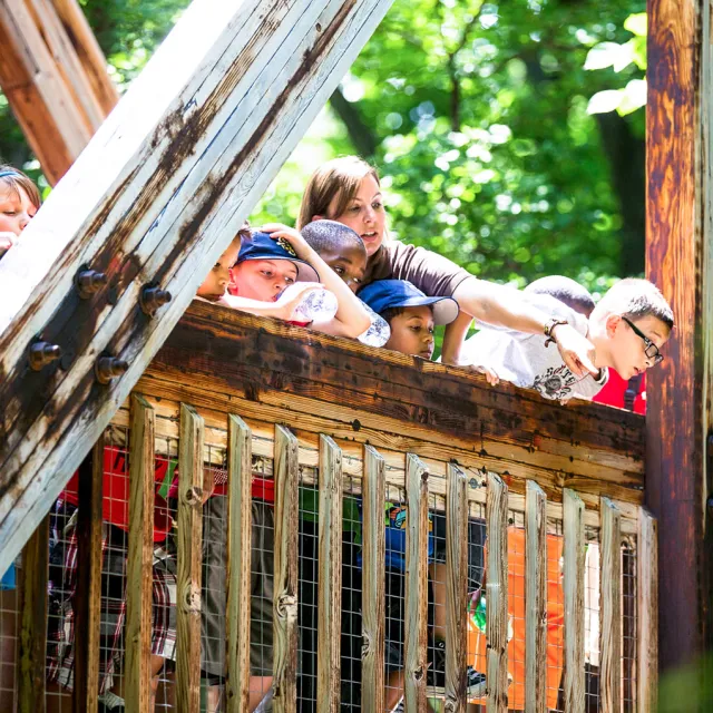 A group of people standing together on a wooden bridge, surrounded by greenery and natural scenery.