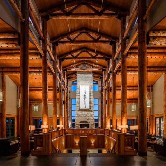 A spacious lodge interior with wooden beams, stone fireplace, and warm lighting, showcasing a serene atmosphere.