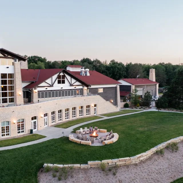 Aerial view of Lied Lodge with a stone facade, surrounded by greenery and a circular fire pit for gatherings.