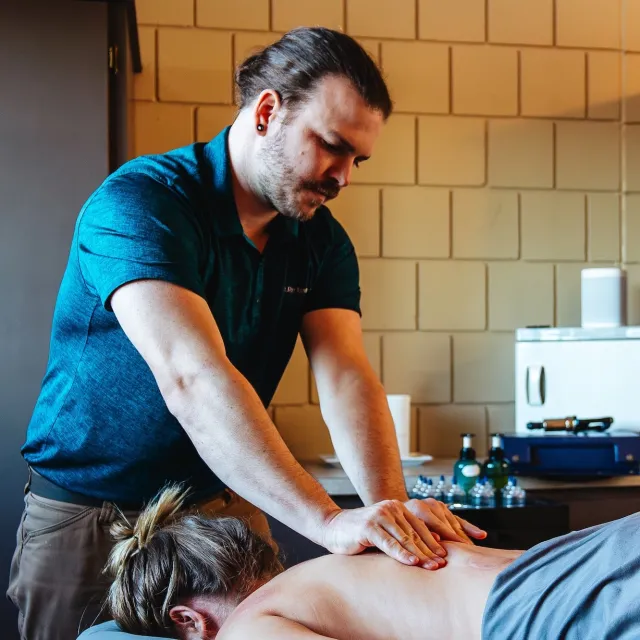 A person receiving a massage while lying face down on a massage table, with a therapist applying pressure on their back.