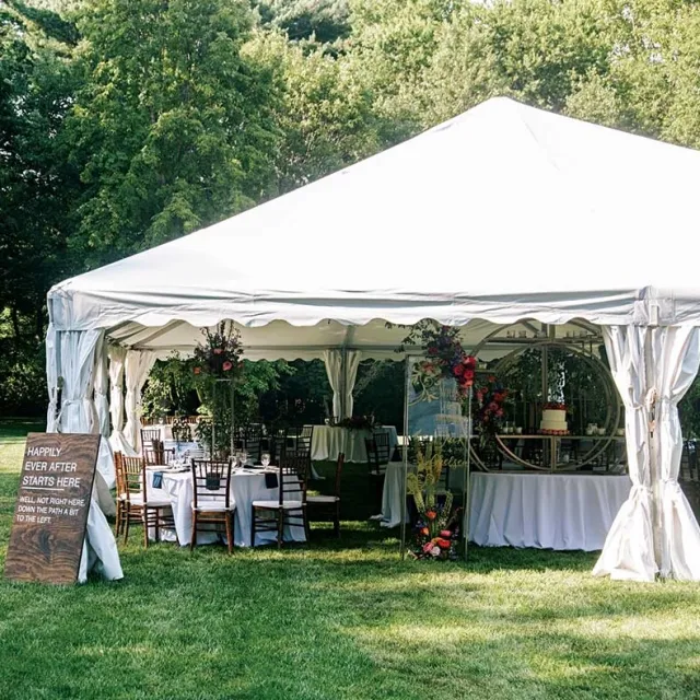 A decorated outdoor wedding tent with elegant tables, floral arrangements, and a sign reading "Happily Ever After Starts Here."