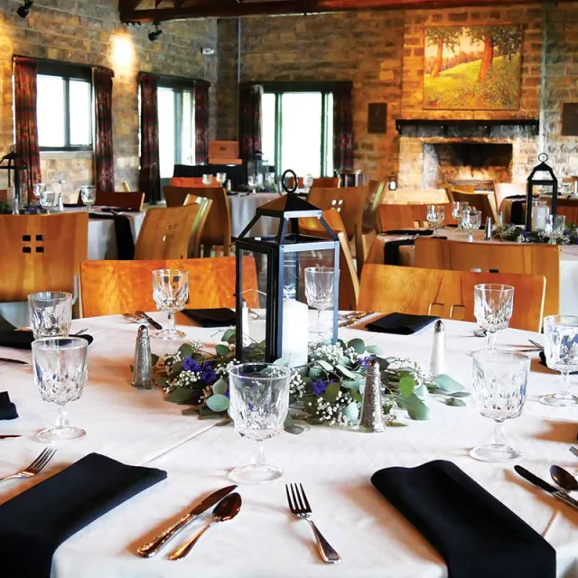 Elegant dining setup featuring tables adorned with white tablecloths, black napkins, crystal glassware, and floral centerpieces.