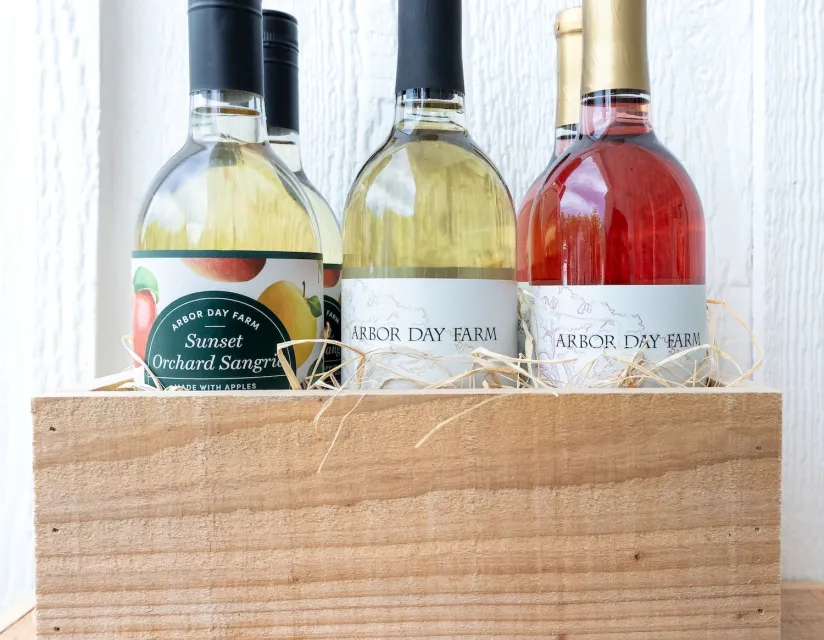 Bottles of Arbor Day Farm wines, including Sunset Orchard Sangria, arranged in a wooden crate with straw accents.