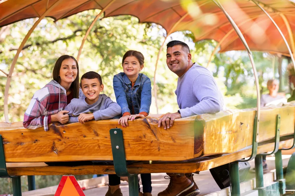 A family enjoying a ride on a tractor, surrounded by lush greenery and bright sunlight.