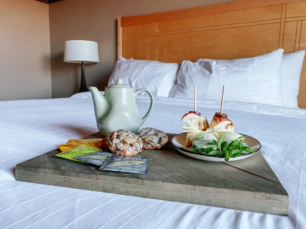A tray with an assortment of food and a cup of tea placed on a neatly made bed.