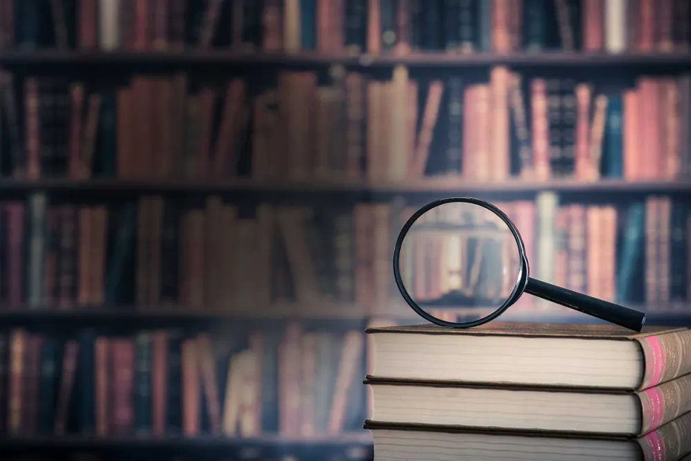 A magnifying glass resting on a wooden bookshelf filled with various books.