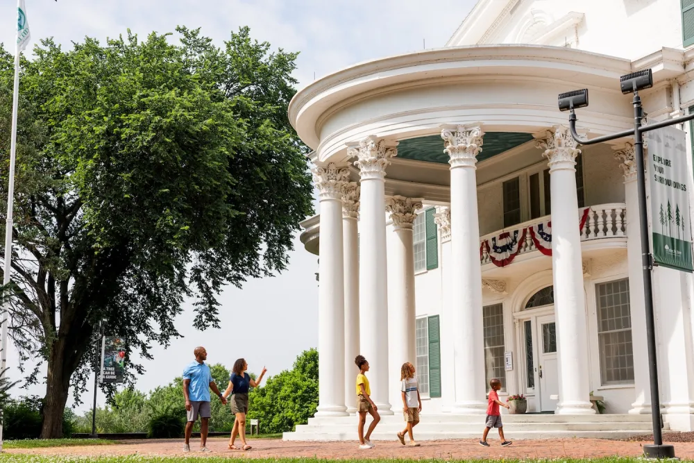 A family walks toward a large white mansion with architectural features.