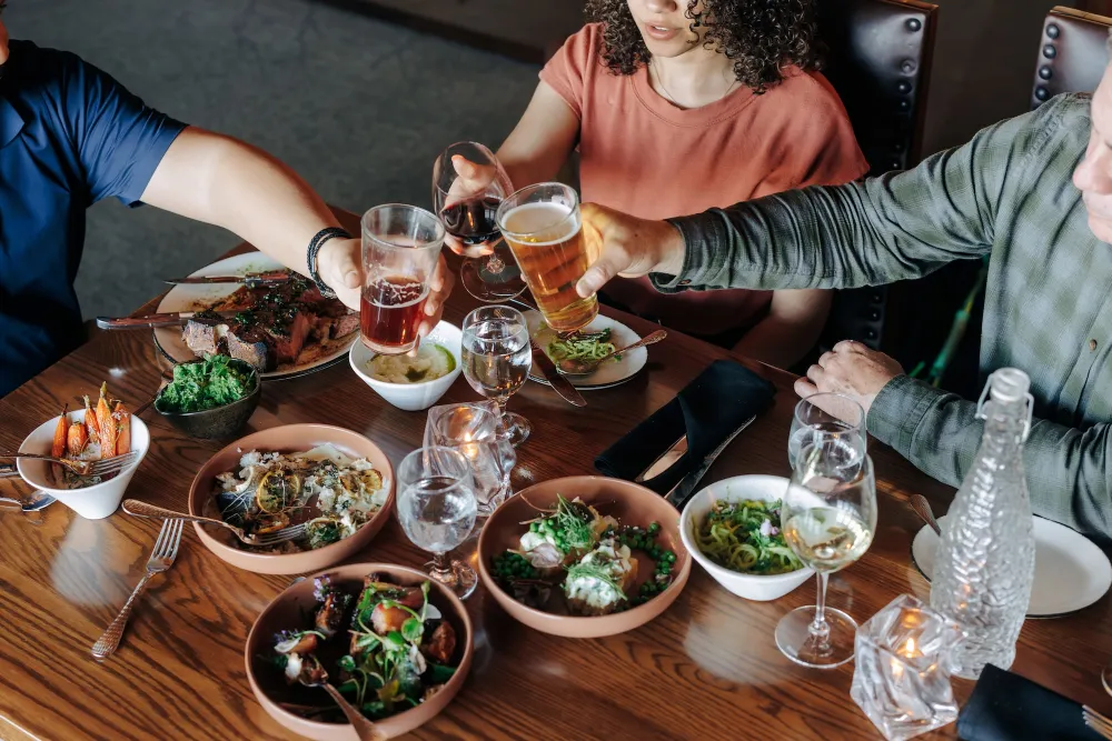 A table filled with various dishes and drinks, as friends raise their glasses for a toast during a lively dining experience.