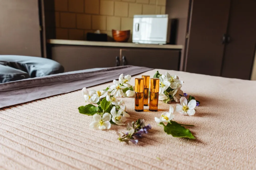Three amber glass vials surrounded by delicate white flowers on a soft beige surface in a serene, spa-like setting.