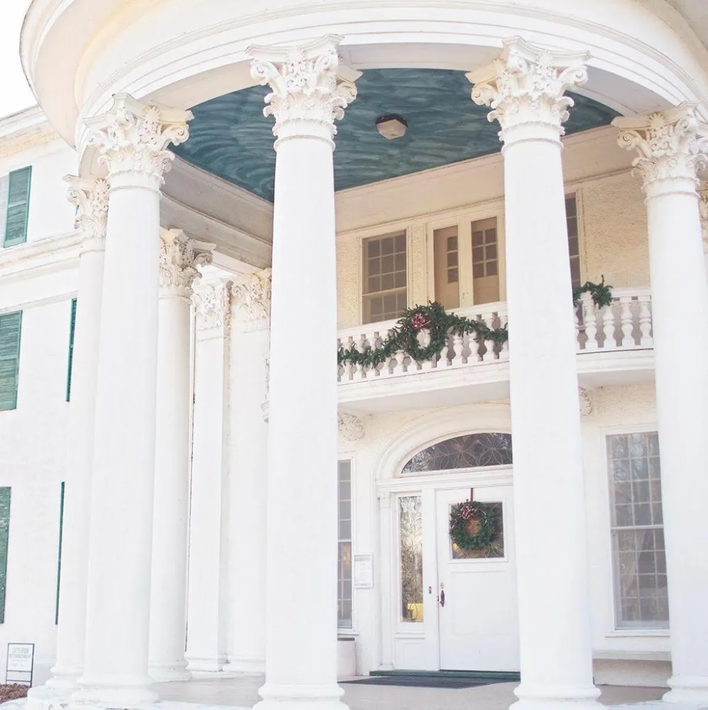 Elegant entrance of a stately building featuring tall white columns, decorative wreaths, and a blue ceiling above the porch.