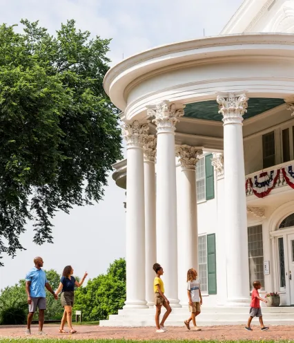 A family walks toward a large white mansion with architectural features.