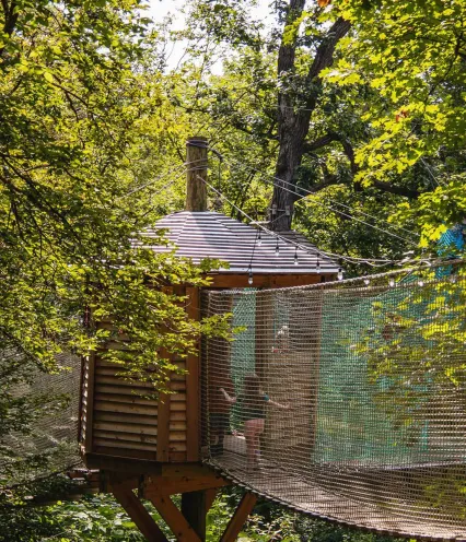 A treehouse surrounded by lush green foliage, connected by a rope bridge. Sunlight filters through, creating a serene and adventurous atmosphere.