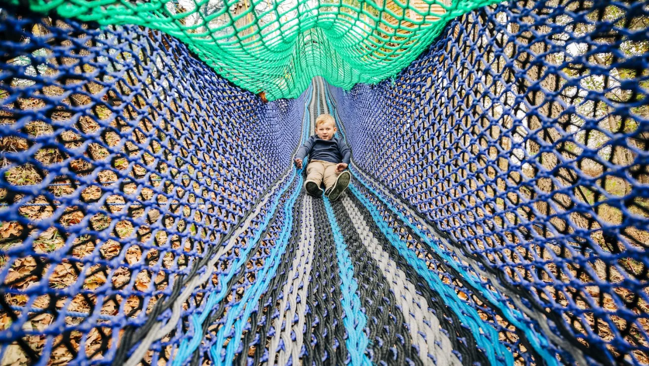 A child sits on a net slide inside a tree house.