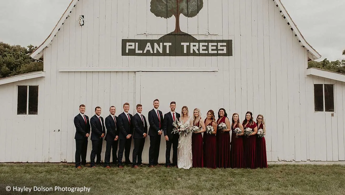 Wedding party in front of plant trees barn