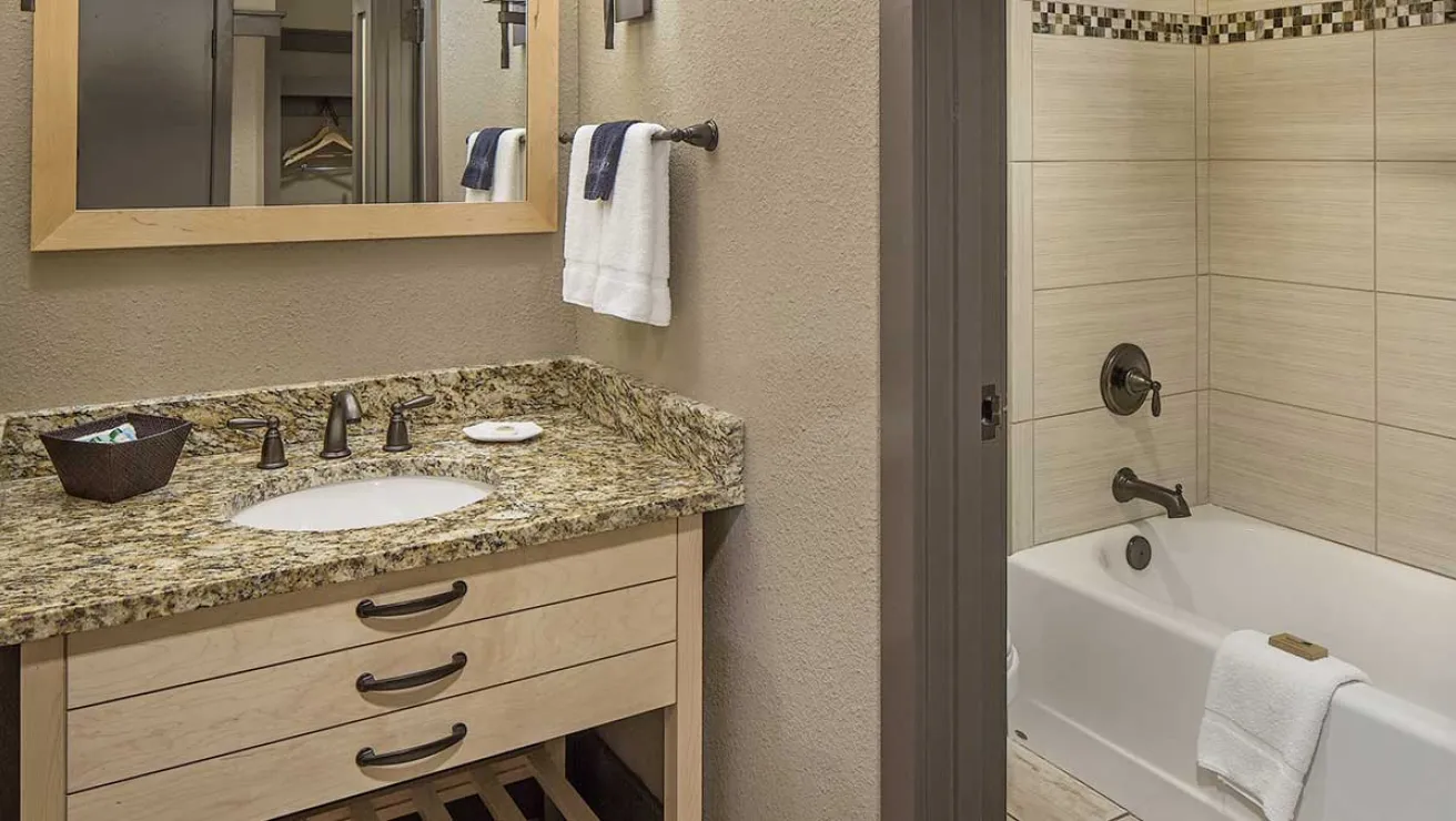 A bathroom featuring a sink, a bathtub, and a wall-mounted mirror reflecting the room's interior.