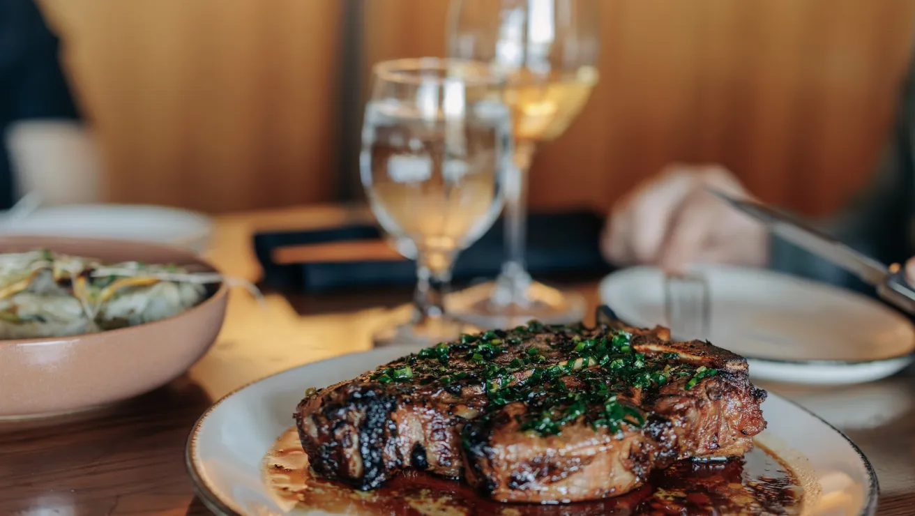 A juicy steak garnished with fresh herbs, served on a plate with wine and water glasses in a cozy dining setting.