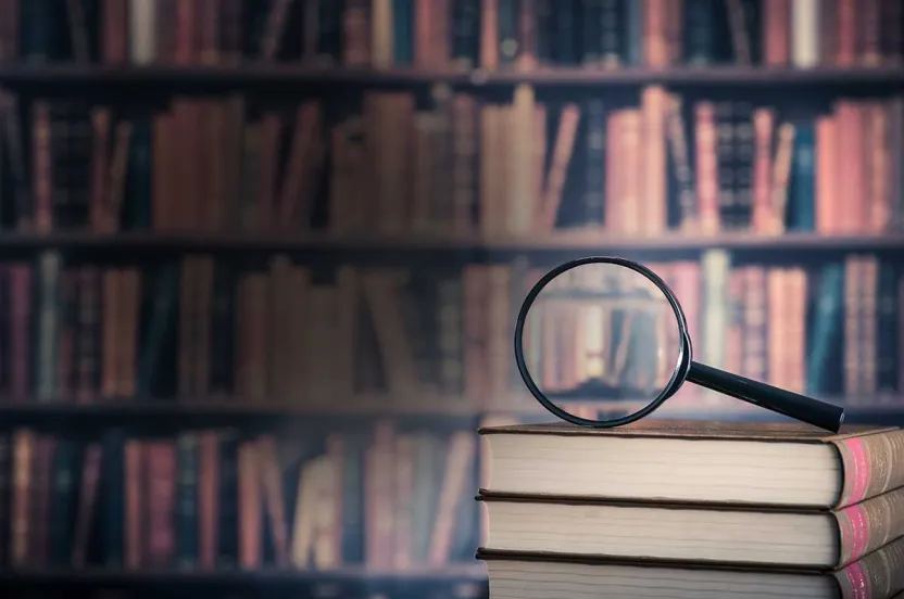 A magnifying glass resting on a wooden bookshelf filled with various books.