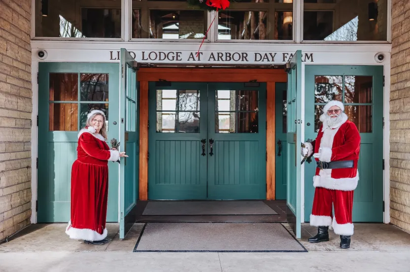 A festive scene at Arbor Day Farm Lodge features a Santa and Mrs. Claus at the entrance, warmly welcoming visitors.