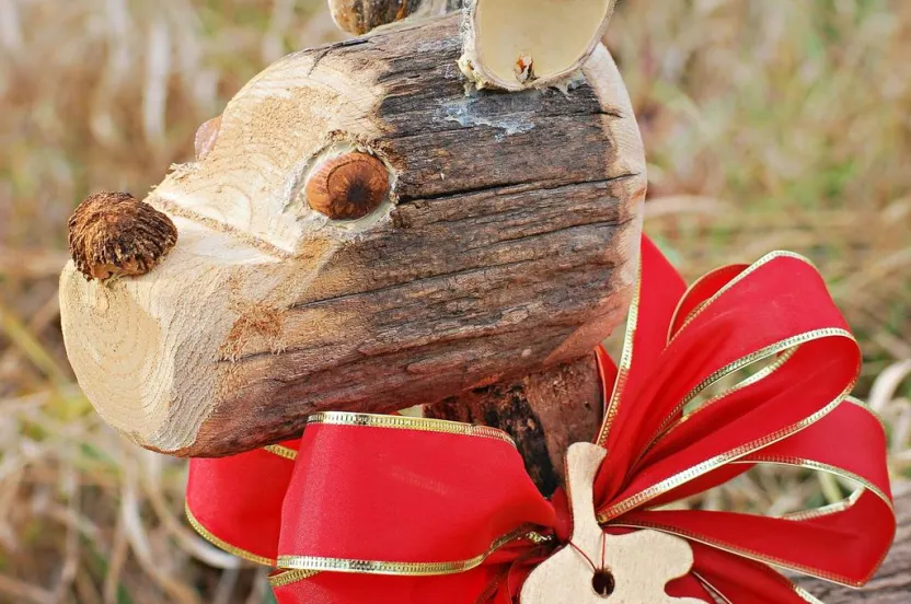 Close-up of a wooden reindeer figure adorned with a red bow and gold trim. A leaf-shaped tag labeled "Cupid" hangs from the bow.