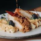 A plate featuring crispy fried chicken atop waffles, garnished with blackberries and drizzled with syrup.