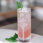A tall glass filled with pink drink and ice, garnished with fresh mint leaves, set on a light marble surface.