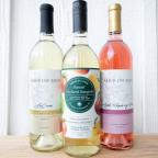 Three bottles of Arbor Day Farm wine: La Crosse (white), Sunset Orchard Sangria (apple), and Apple Raspberry Wine (pink), displayed on a wooden surface.