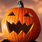 A carved Halloween pumpkin with a jagged, toothy grin and sharp eyes, illuminated against a softly blurred orange background.